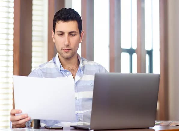 Business user checking VAT details on a document beside a laptop